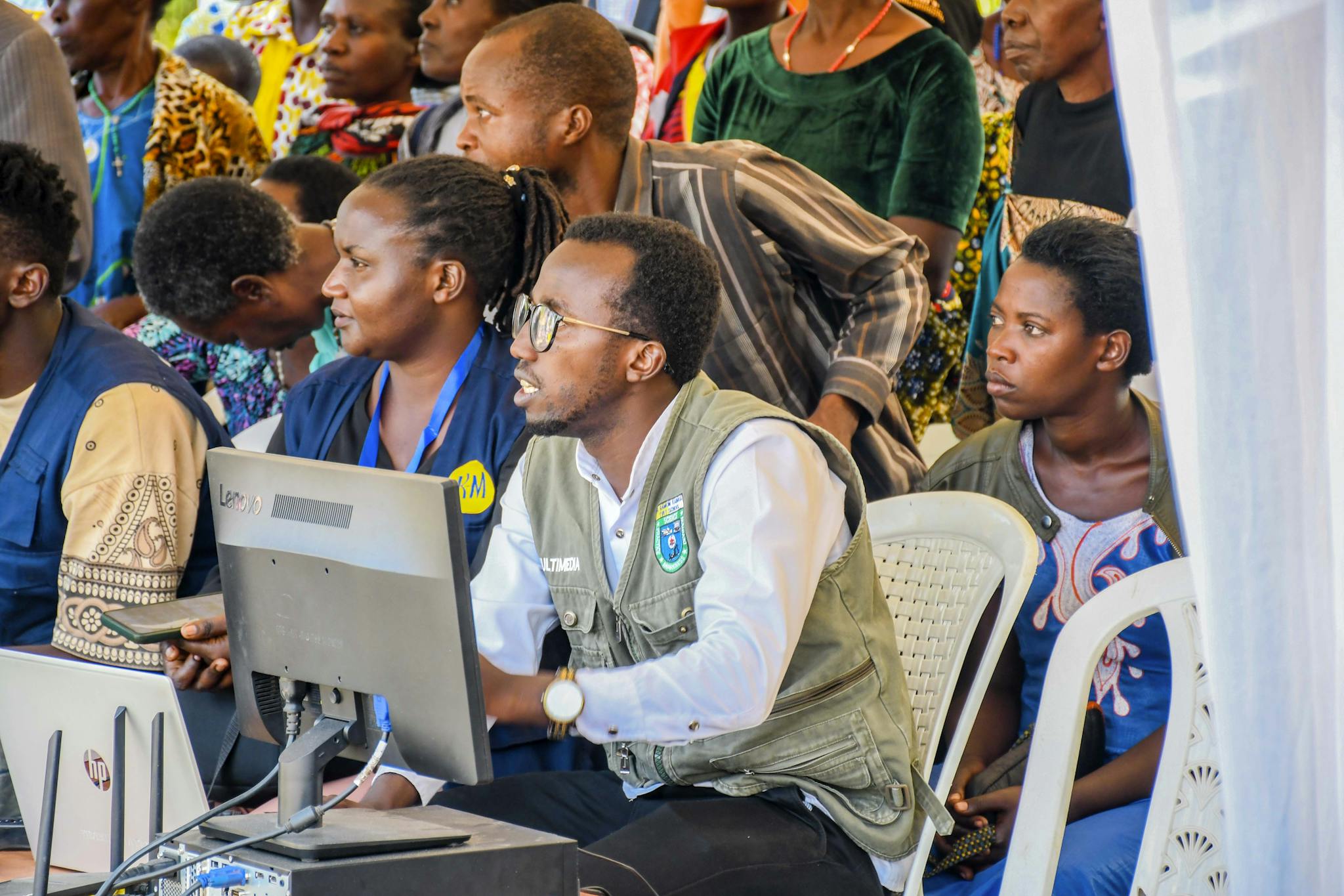 A diverse group of adults engaging with technology at a community event in Rwanda.